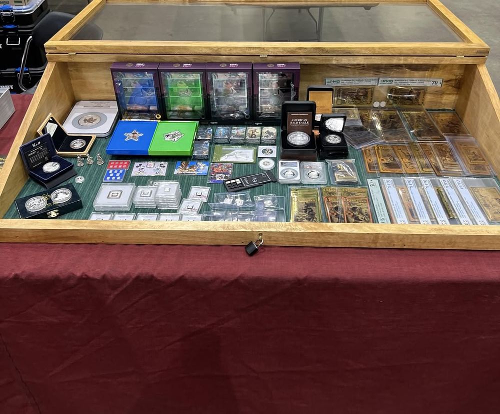 PJ's display case at a coin show, filled with slabbed coins, bullion and notes